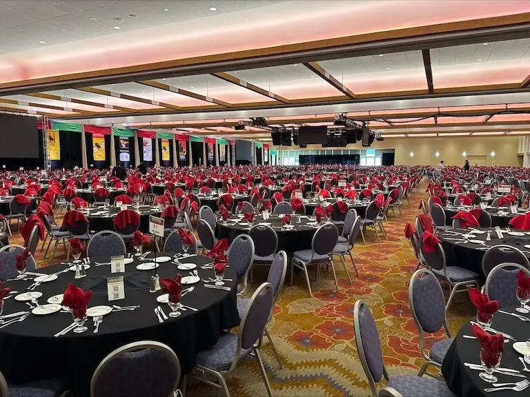 Banquet room set up with round tables with black tablecloths and red napkins sticking up out of the glass at each place setting.