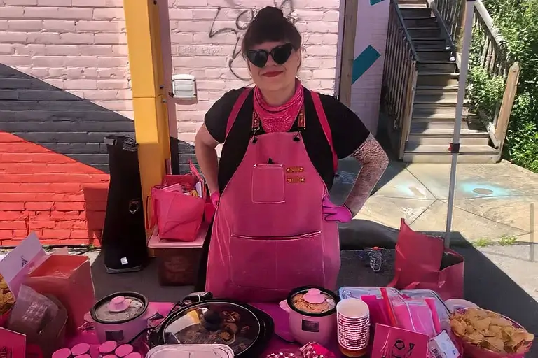 Chef Bree Chumley standing behind a table filled with handmade vegan dishes and spices.