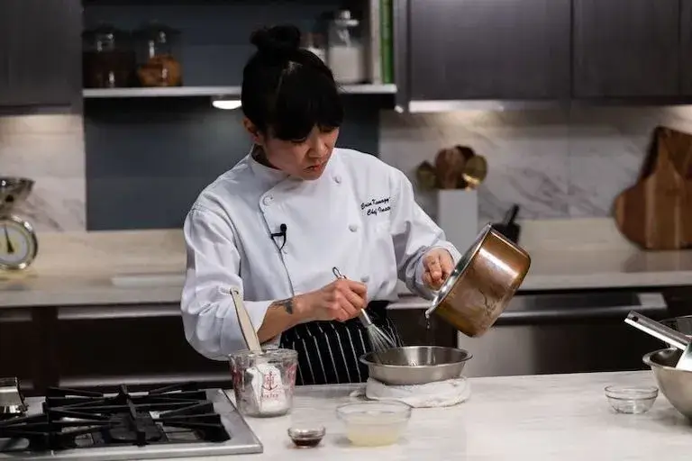 Chef Instructor whisking ingredients while pouring liquid from a saucepan.