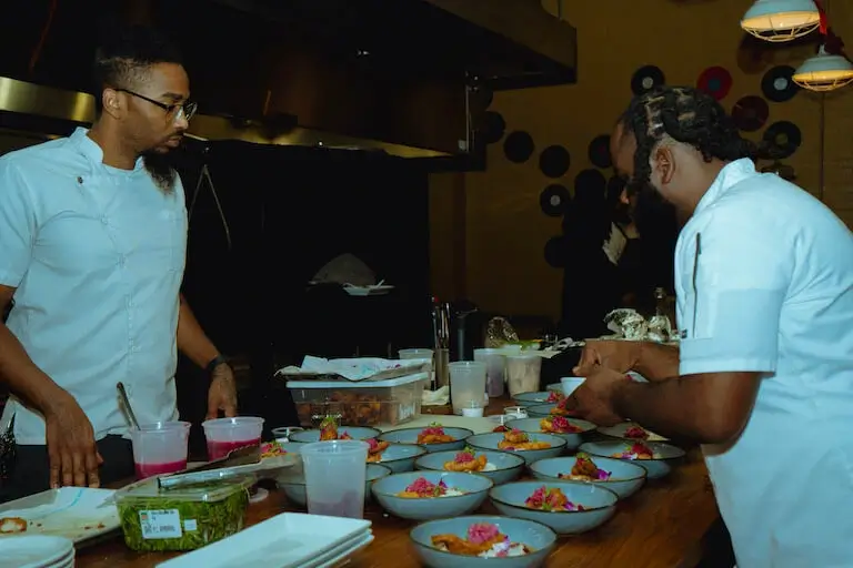 Chef Rodney Smith plating food alongside Chef Demetrius Brown in a professional kitchen.