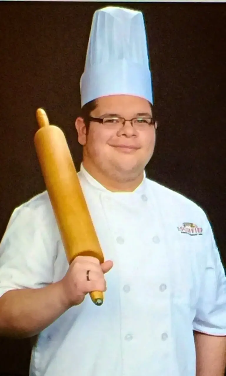 Christopher Puga wearing a white chef coat with the Escoffier logo and holding a rolling pin to his shoulder.