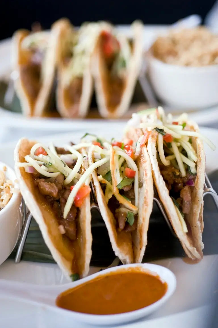 Close-up view of three Korean beef tacos and a white ladle with sauce.