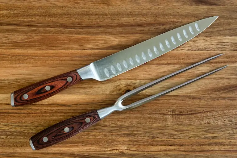 Closeup of a carving knife and fork on brown background.