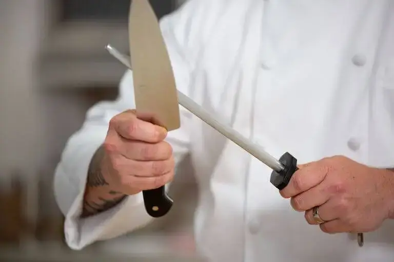 Closeup of a chef using a honing rod to sharpen a knife.