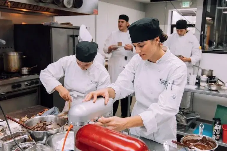 Culinary students working with stand mixers and melted chocolate in a pastry class.