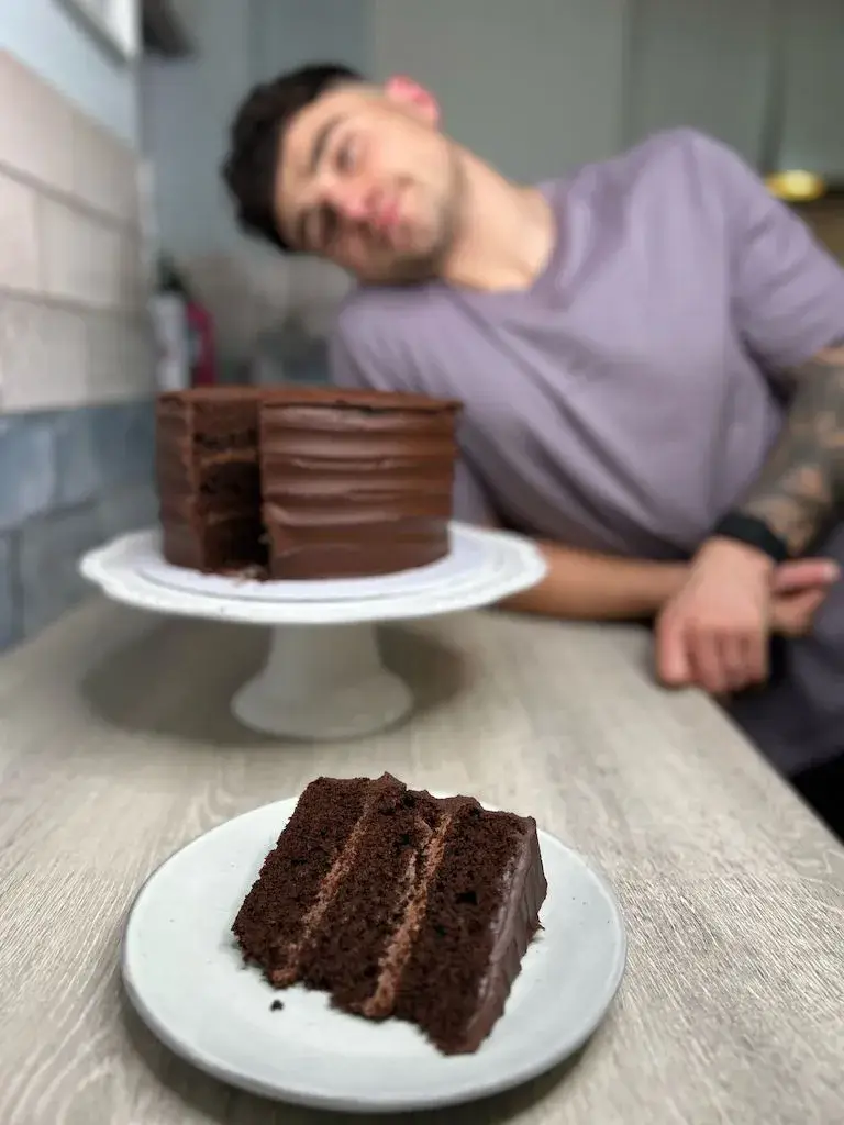 Frosted chocolate layer cake with slice cut out with Matty Edgell in the background.