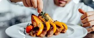Chef garnishing grilled meat with roasted potato slices and fresh herbs