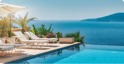 Infinity pool at a resort overlooking the ocean with lounge chairs and tropical plants
