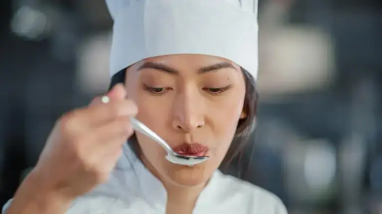 Chef tasting food from a spoon while working in a professional kitchen.
