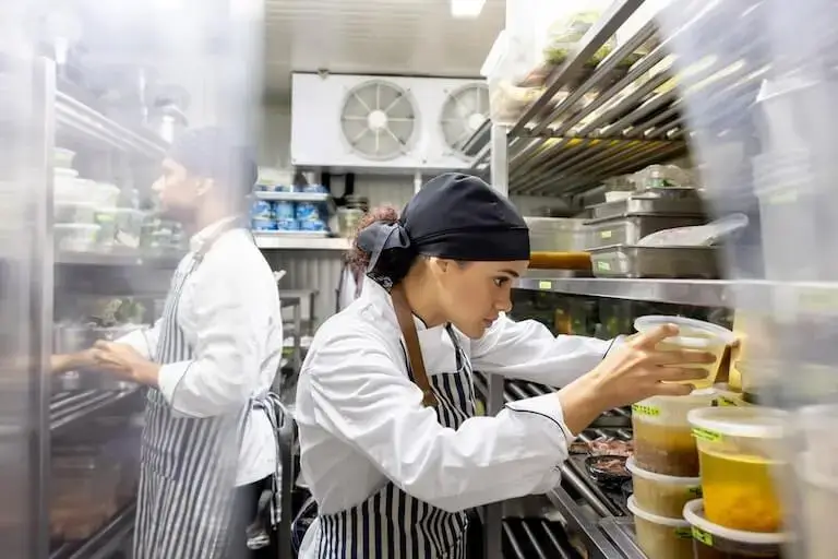 Chefs organizing ingredients and containers in a busy restaurant kitchen.