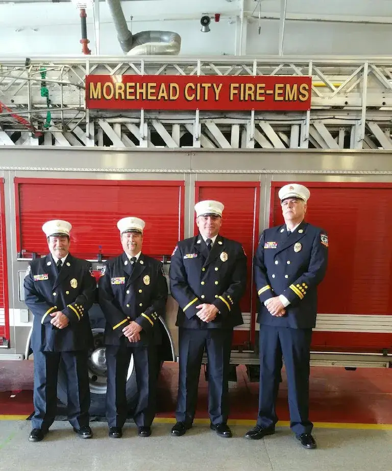 Kevin Fuller standing with three other uniformed firefighters in front of a fire truck labeled “Morehead City Fire-EMS.”