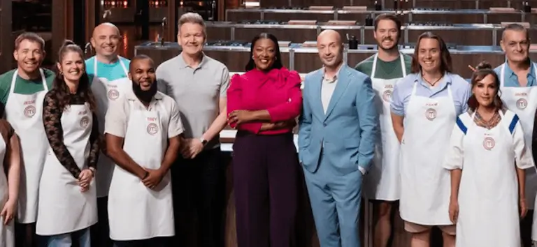 Kevin posing with the MasterChef cast, judges, and co-competitors on set in aprons.