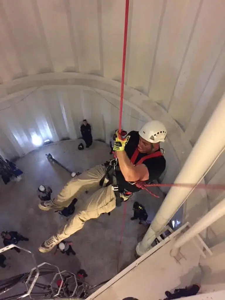 Kevin rappelling down a tall structure in full safety gear during fire and EMS training.
