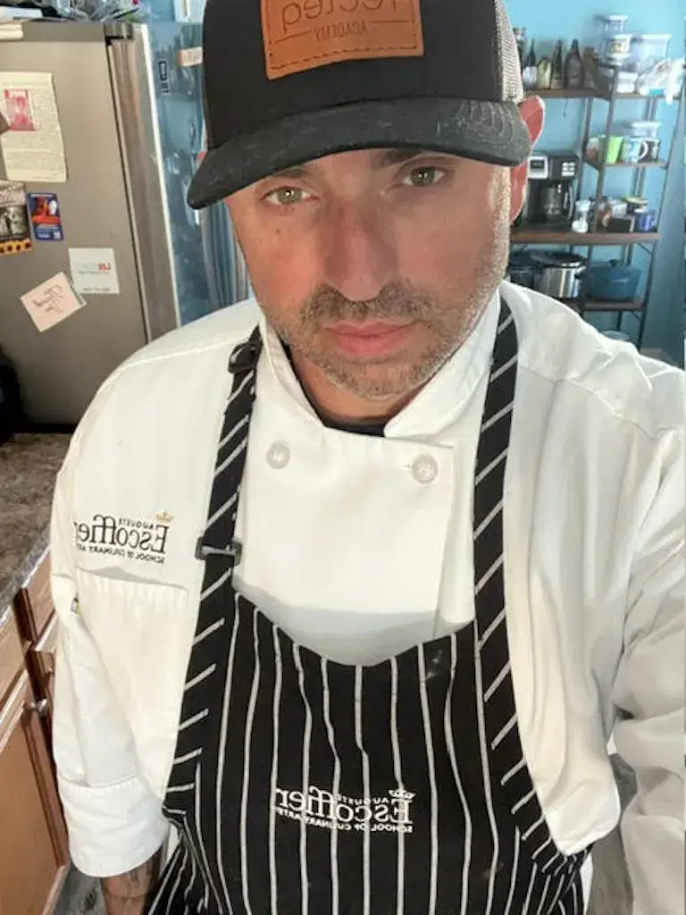 Kevin wearing an Escoffier chef jacket and apron, standing in his home kitchen.