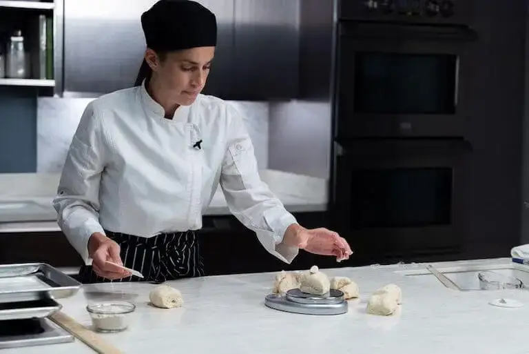 Pastry student dividing dough with a scale in a kitchen classroom.