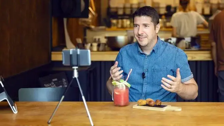Person filming a food video at a cafe with a smartphone tripod and drink setup.