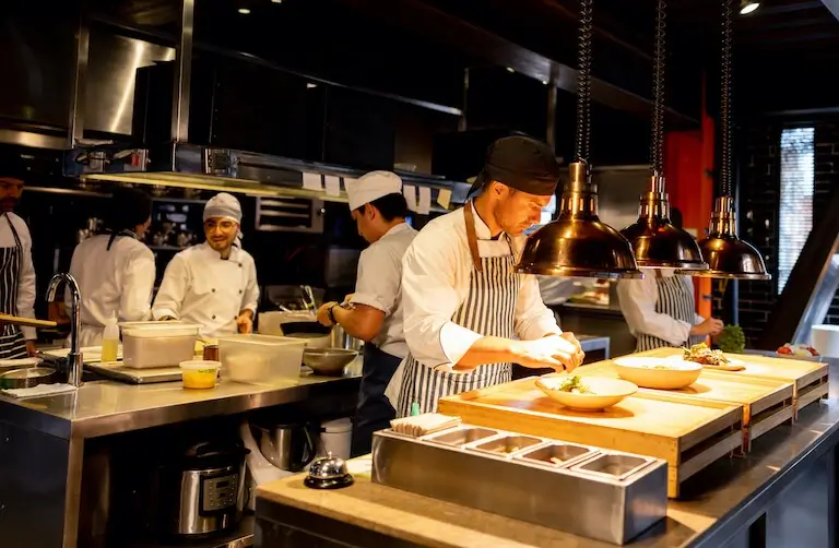 Professional kitchen team working together during dinner service, with chefs focused on plating dishes under warm pass lights.