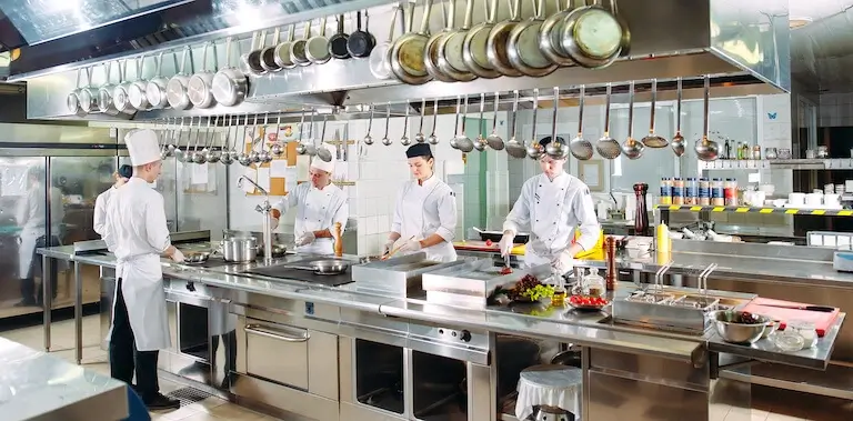 Several people in chef’s uniforms work side by side in a brightly lit restaurant kitchen.