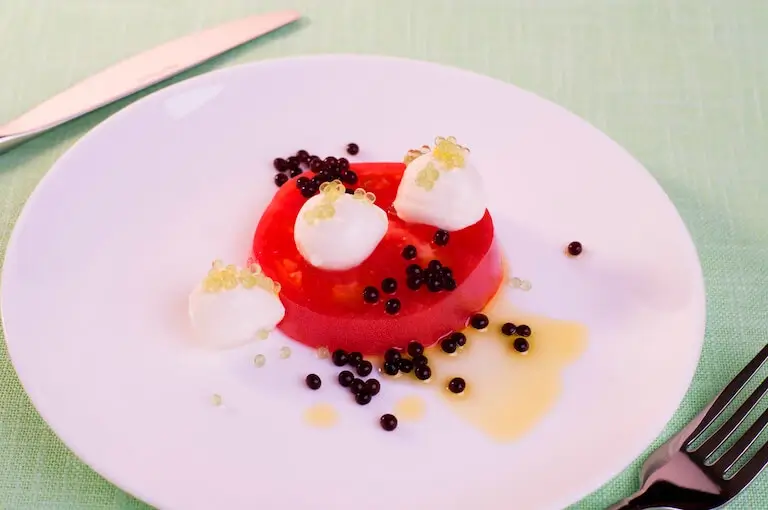 Tomato slice topped with mozzarella and balsamic pearls created through spherification.