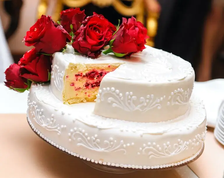 Two-tiered white frosted wedding cake with piped swirls and a slice missing showing fruit filling inside.