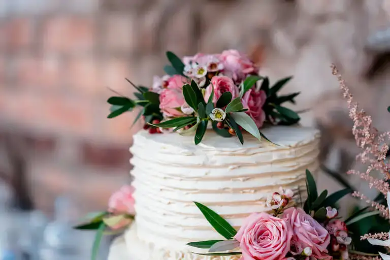 Wedding cake with white frosting decorated with pink roses and greenery.