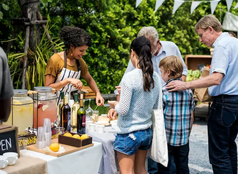 Woman serving food and drinks at an outdoor festival stand, interacting with attendees.
