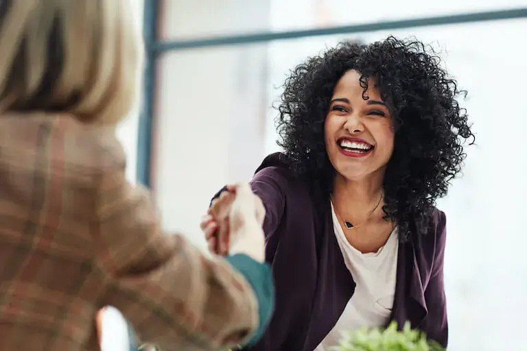 Woman smiling and shaking hands during a professional interview.